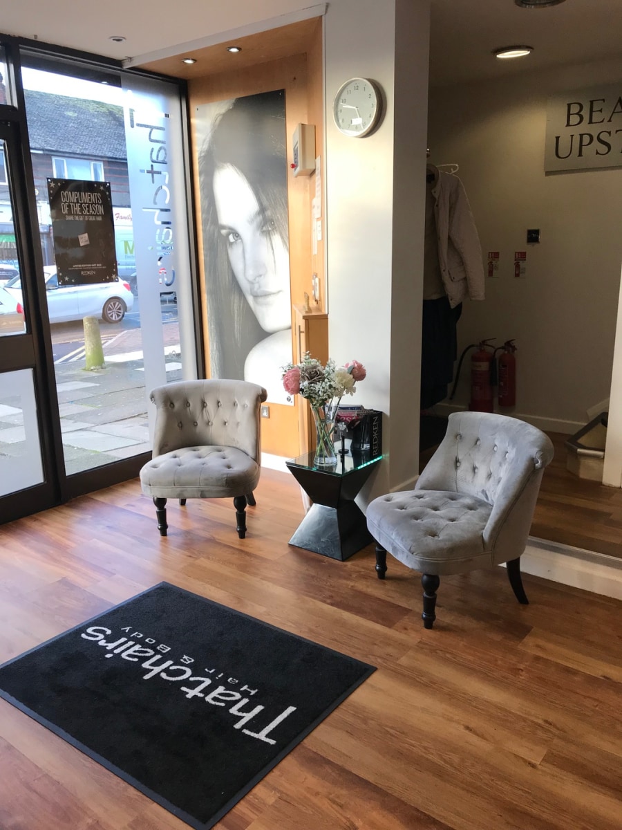 The reception at Thatchairs Hair & Body in Huyton, with two grey velvet chairs, fresh flowers and the Thatchairs doormat